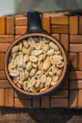 Crunchy, fried and salted peanuts, peeled. A nutritious snack in a small kerimic pot on the background of a natural brown tree with a natural pattern. Appetizing dish in the fresh air.