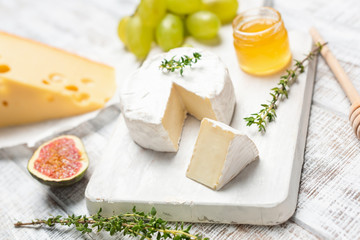 Brie or camembert cheese on white wooden board served with honey, green grapes and figs