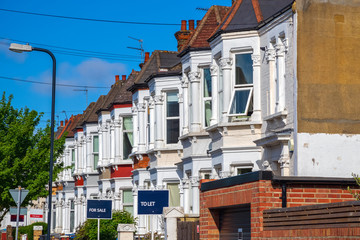 A row of typical British terraced houses in London with estate agent boards