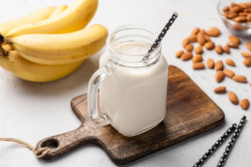 Banana protein smoothie in drinking glass on wooden serving board. Closeup view