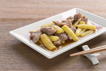 stir fried baby corn and pork with oyster sauce in a plate on wooden table. asian homemade style food concept.