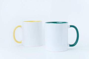 Two white mugs, with a green and yellow handle on a white background.  Isolated.  