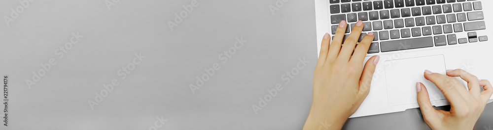 Wall mural website banner of top view laptop keyboard and female hands with copyspace in grey color background.