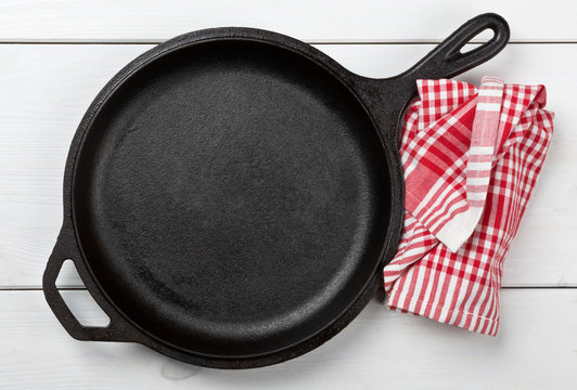 Empty, clean black cast iron pan or dutch oven top view from above on white table with towel