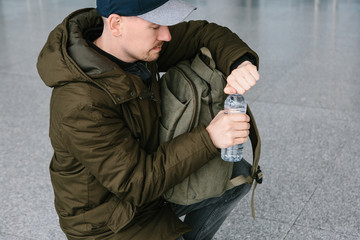 The traveler opens a bottle of water to drink. A person is going to make a rest.