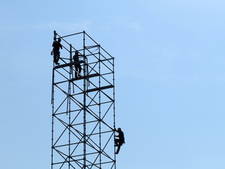 Silhouettes of construction workers on scaffolding. Builders on the background of clear blue sky, building works