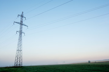 Supports high-voltage power lines against the blue sky on sunrise. Electrical industry.