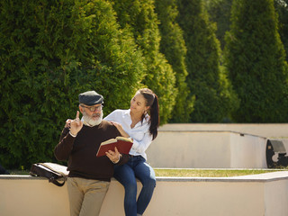 Help someone you love. Portrait of young smiling girl embracing grandfather with book against city park. community and family lifestyle concept