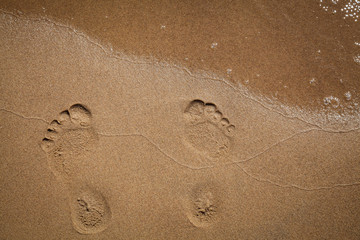 Footprints of bare feet in the sand along a river bank with an oncoming wave