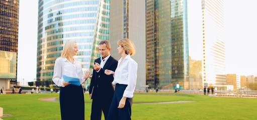 Beautiful businesswomen keeping blue document case talking with cheerful male boss outside. Concept...