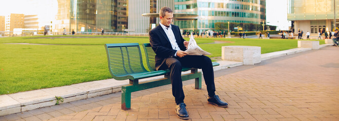 Businessperson reading newspaper and looking at watch outdoors in  . Concept of having break,...