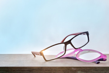 Two eyeglasses on wood table with blue background