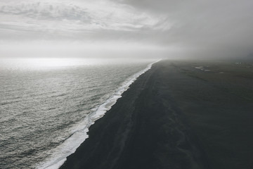 wavy ocean and coastline of black sand beach under cloudy sky in Vik, Iceland