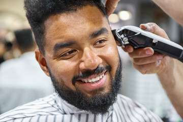 Happy black man in barbershop. Barber shaving cheerful African guy in male beauty salon