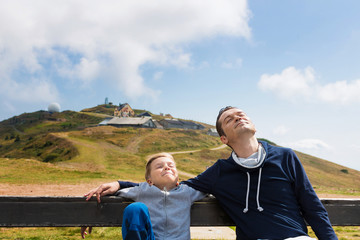 Happy father and son relaxing with eyes closed on top of the mountain.