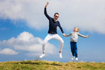 Joyful father and son holding hands and jumping against the sky.