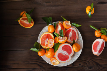 Fresh juicy fruit oranges, tangerines, persimmon, grapefruit on a white plate in a cut closeup on a dark textured wooden background. Background and place for text, inscriptions