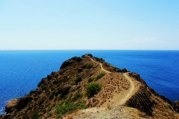 View from the top of the mountain to the Black Sea and to Cape Rybachiy. A narrow path runs along the edge of the cape. Republic of Crimea