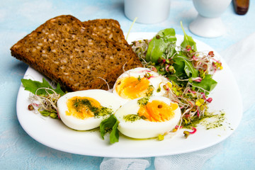 Healthy breakfast: Hard boiled eggs, fresh radish sprouts, arugula and dark whole wheat  bread with herb sauce, on blue background