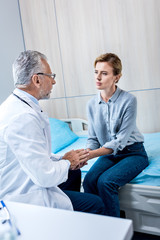 Obraz premium mature male doctor holding hands of female patient in hospital room