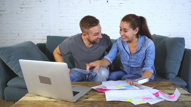 Happy Young Couple Paying Bills Together And Managing Budget, Sitting On The Sofa And Using Calculator And Laptop In Financial Concept