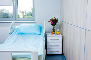 interior of hospital room with bed, flowers and nightstand