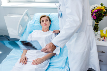 cropped image of male doctor holding x-ray picture and cheering up female patient in hospital room