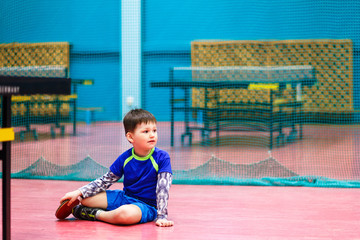 boy in sports uniform sits on the floor in the gym