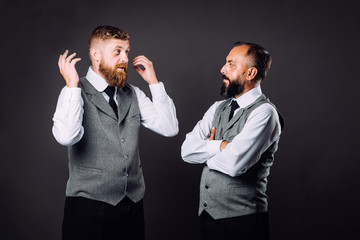 Two bearded men in suits talking and gesticulating to each other on black