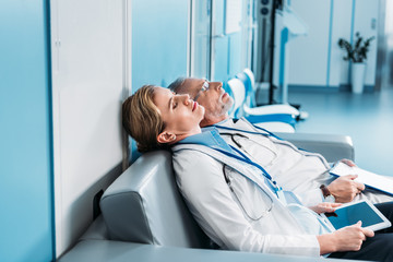 side view of tired male and female doctors sleeping with clipboard and digital tablet with blank...