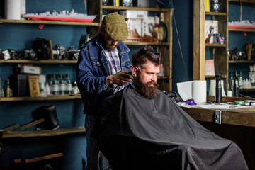 Hipster client getting haircut. Barber with hair clipper works on haircut of bearded guy barbershop...