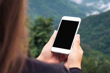 Mockup image of a woman holding white smart phone with blank desktop screen in outdoor with blur green mountains background