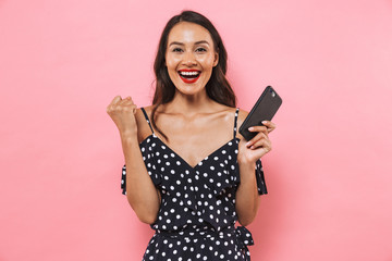 Naklejka premium Cheerful young woman isolated over pink background using mobile phone.