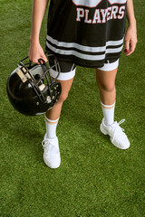 Fototapeta premium cropped shot of woman in american football uniform holding helmet while standing on field