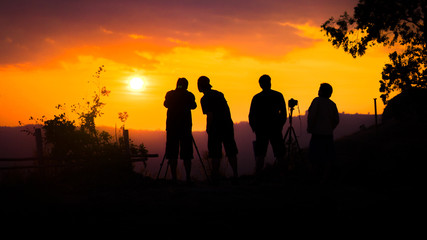 Silhouette of group of friends standing and watching sunset on mountain in evening.