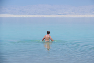 A young attractive man swims in the dead sea without the help of hands, showing how much water is dense