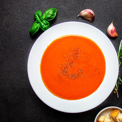 Tomato Soup with herbs on black slate table. Fresh homemade cream of Tomatoes soup with a swirl of cream. Top view.