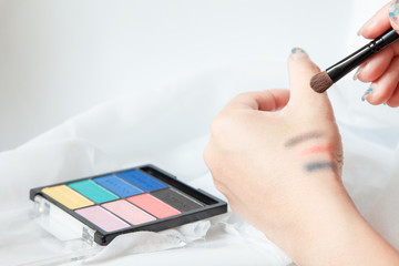 Woman applying Test cosmetic pearlescent shades Colorful eye shadows with a brush for application on hands . Beauty And Make-up Concept