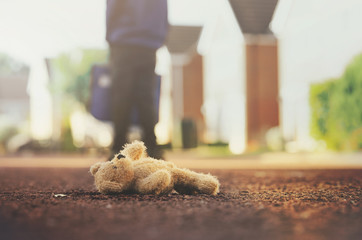 Teddy bear laying on the road with blurry background of school kid carrying school bag,Lonely brown...