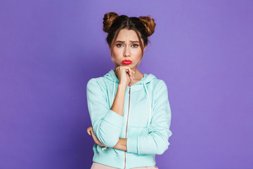 Portrait of upset woman with two buns pouting and looking offended, isolated over violet background...