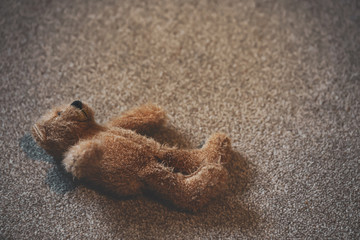Fototapeta na wymiar Teddy bear is laying down on carpet in retro filter, Old teddy bear abandoned ,lonely concept, international missing children's day.