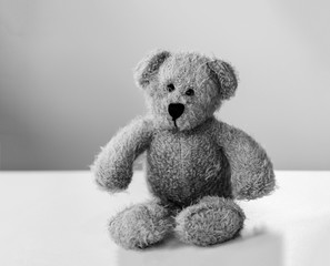 Black and white photo of teddy bear sitting alone on white table with yellow background, One brown bear toy with with copy space