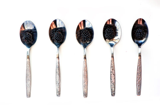 Berries of blackberry lie in tablespoons against the background of white color