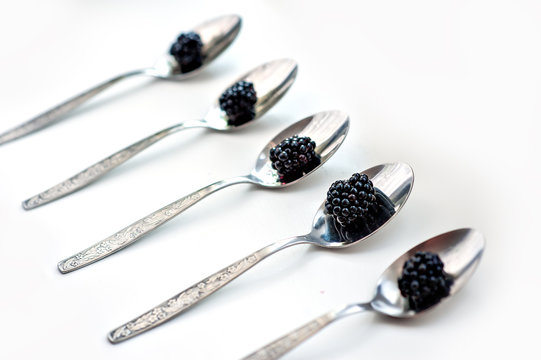 Berries of blackberry lie in tablespoons against the background of white color