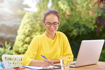 Young woman doing some paperwork and using laptop outside at her garden terrace. 