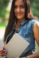 Young pretty brunette girl with the tablet and listening to music on the street in summer.