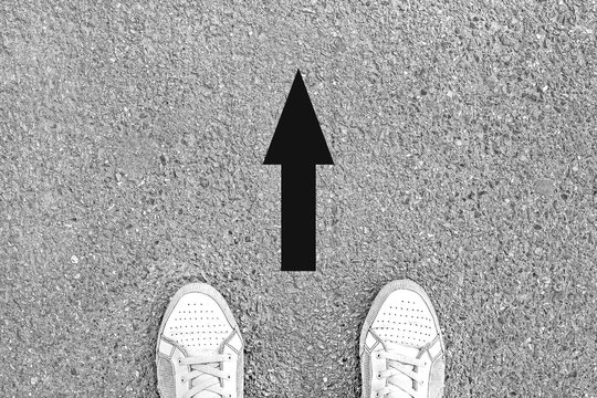 Legs sneakers on pavement, the arrow shows the direction