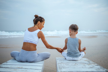 A mother and a son are doing yoga exercises at the seashore of tropic ocean