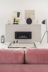 Posters above fireplace in white apartment interior with black lamp and pink settee. Real photo
