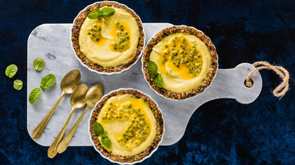 banner of vegan raw mini tarts from nuts and dates with cashew cream from mango purée with lime juice and seeds of passion fruit. healthy alternative food on a blue background